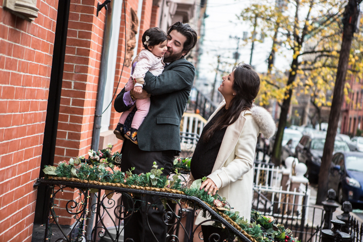Two adults smile with a child outside a brick townhouse.