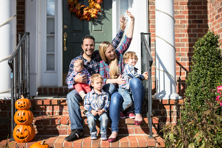 Two adults and three children sit on front steps decorated with pumpkins.