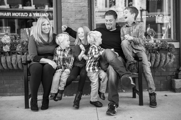 Two adults and three children sit together on a street bench in black and white.