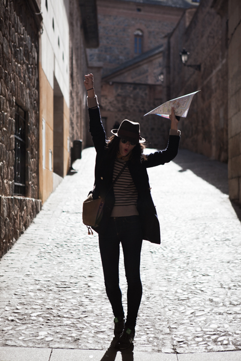 A woman in a dark coat walks along a narrow cobblestone street.