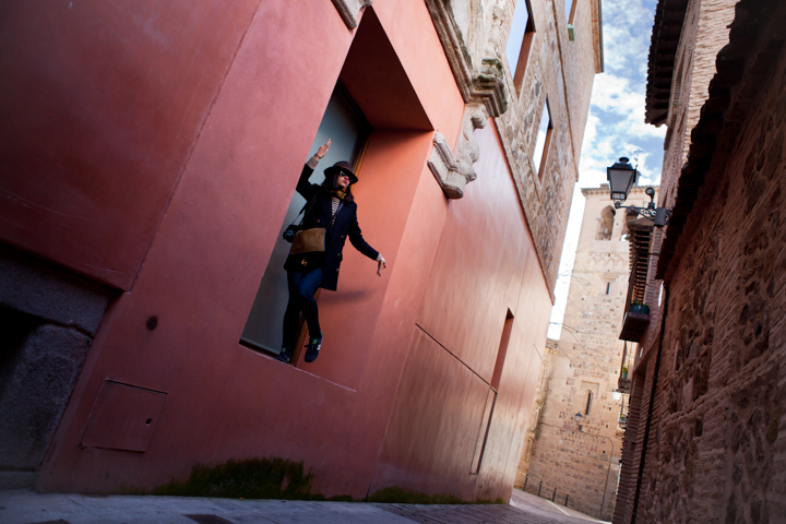 A woman leans out from a colorful wall above a narrow street.