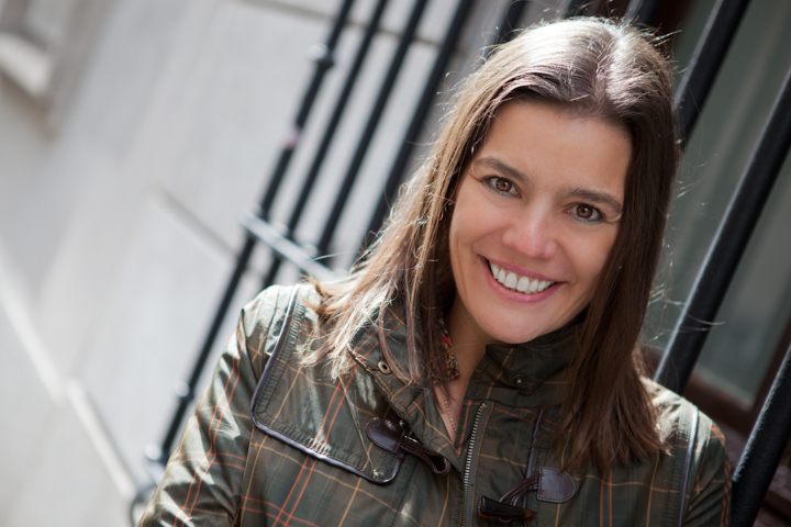 A smiling woman in a patterned jacket beside a building entrance.