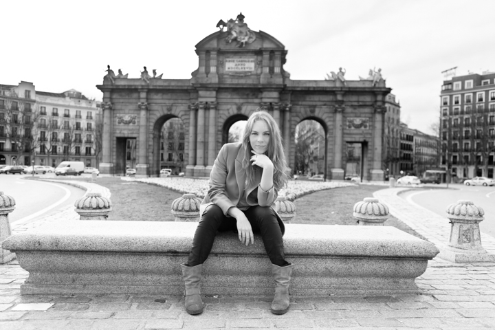 A woman sits on a stone fountain in a grand city square.