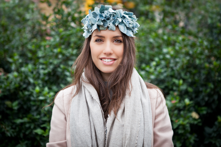 A woman wearing a blue flower crown in a leafy garden.