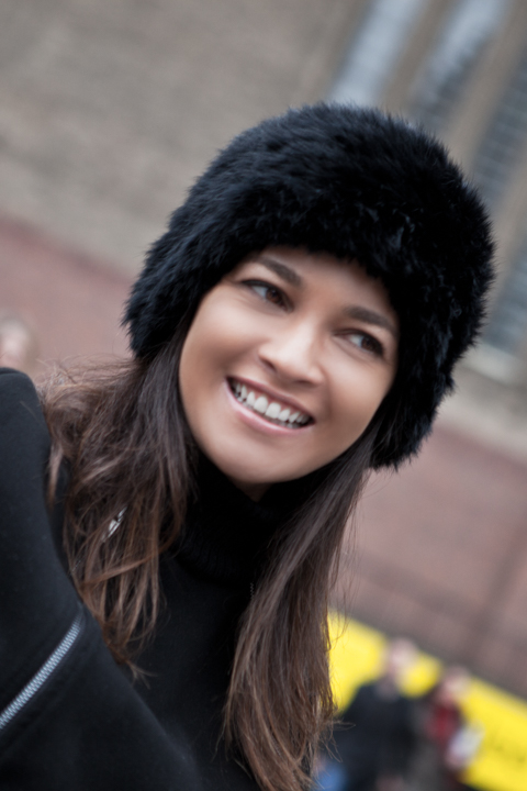 A woman in a black fur hat tilts her head and smiles.