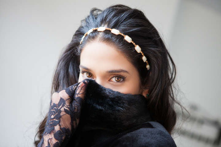 A woman with a jeweled headband holds her dark collar near her face.