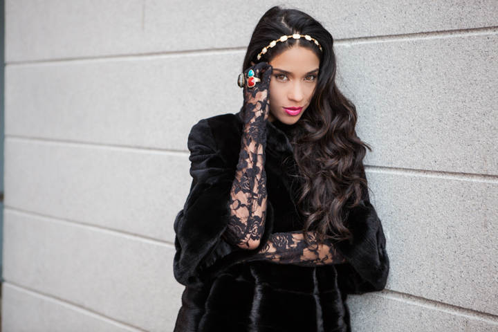 A woman in black lace poses against a stone wall.