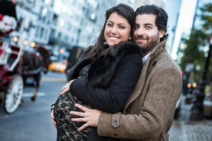 A man hugs a smiling pregnant woman on a city street.