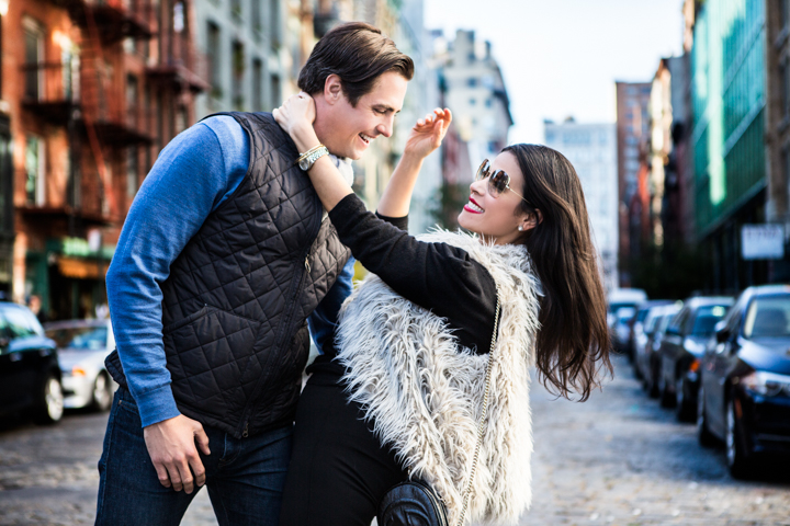 A woman playfully reaches toward a man's hair on a city sidewalk.
