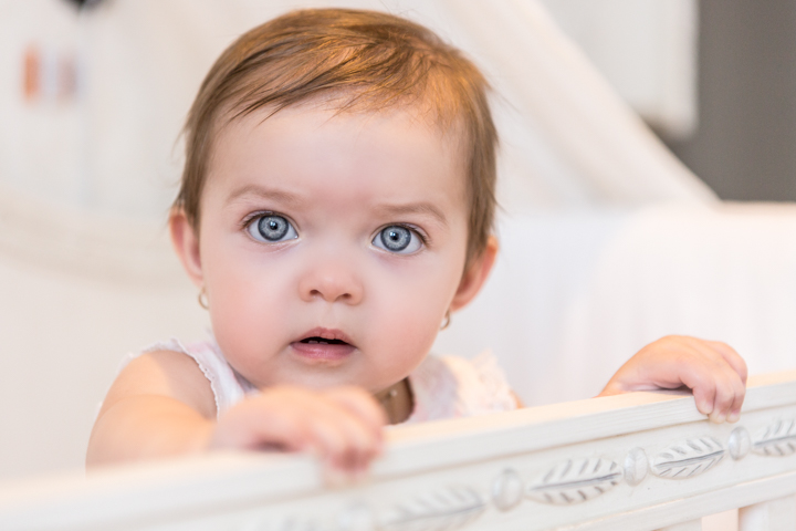 A baby peers over the edge of a pale crib.