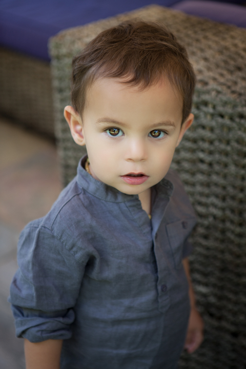 A young child in a blue shirt stands beside a sofa.