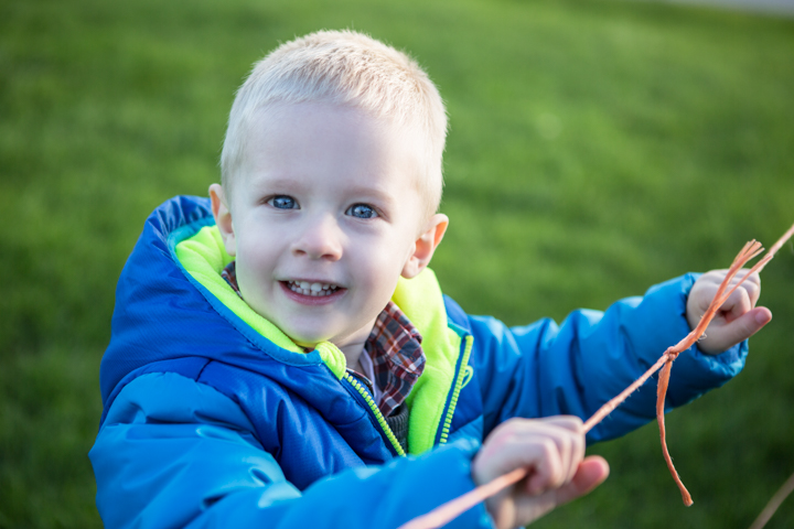 A smiling child in a bright blue jacket holds small twigs outdoors.
