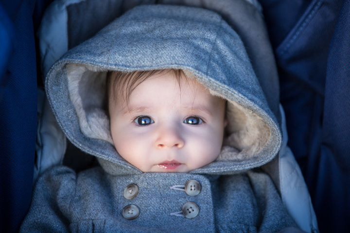 A baby in a blue hood sits snugly in a stroller.