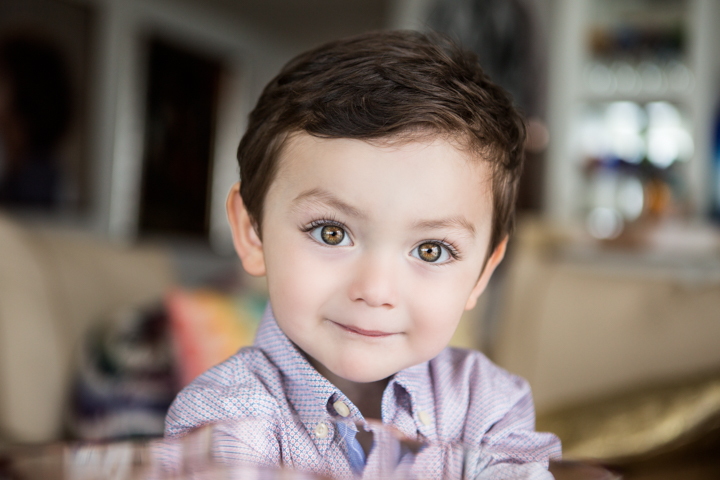 A smiling child in a checked shirt looks toward the camera indoors.