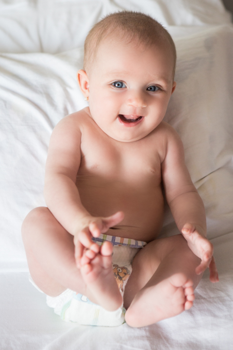 A smiling baby sits on a soft white bed.