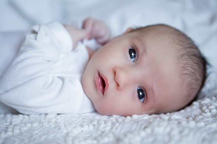 A newborn in white lies on a soft textured blanket.