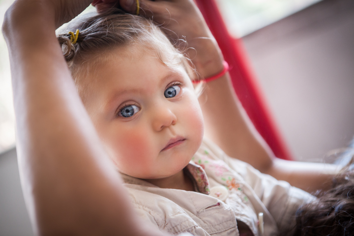 A young child with small hair clips sits indoors beside an adult.