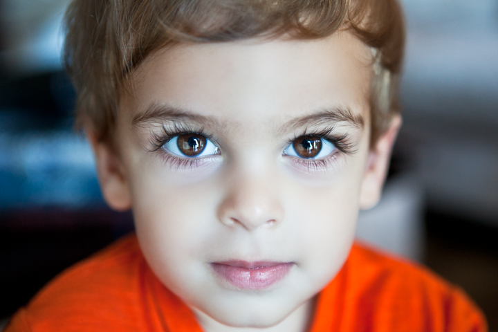 A child in an orange shirt looks toward the camera in a close-up portrait.