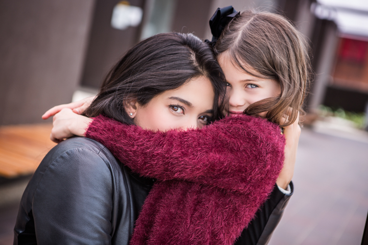 A woman and child cuddle behind a thick red scarf.