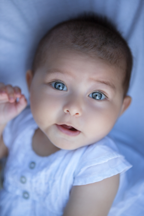 A baby in a pale blue outfit lies on soft bedding.