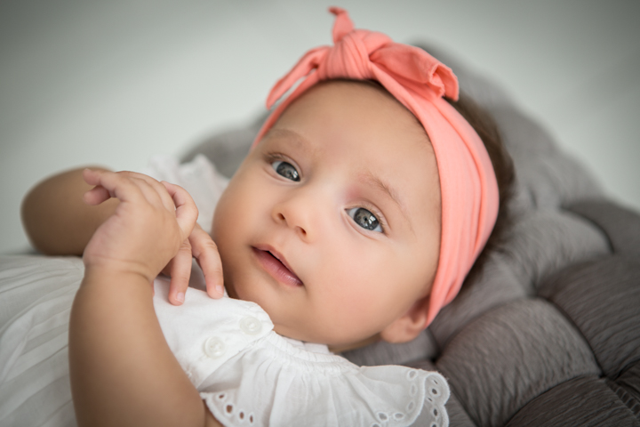 A baby with a pink bow headband rests against an adult's arm.