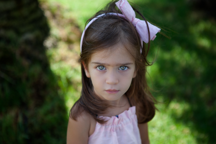 A child with a purple hair bow stands among green garden plants.