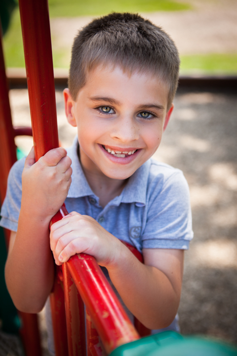 A smiling child in a blue shirt holds onto colorful playground bars.