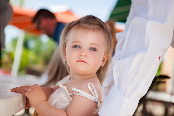 A toddler in a white top sits at an outdoor table.