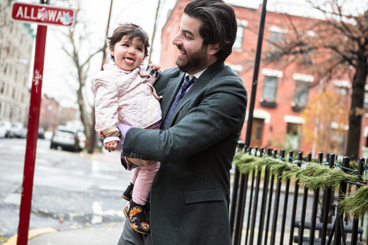 A man holds a laughing child on a city sidewalk.