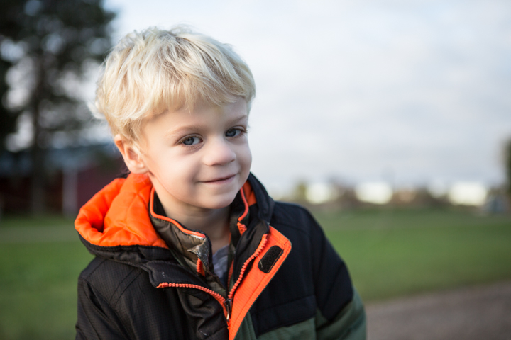 A child in a dark jacket with orange lining stands in an open field.