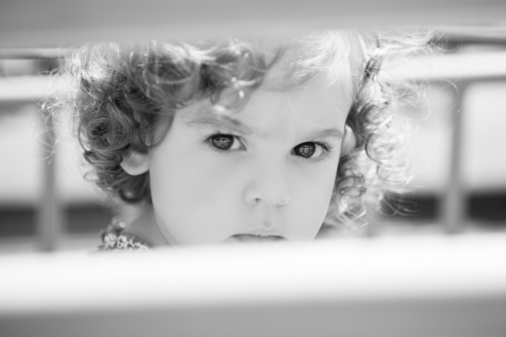 A curly-haired child peers over a surface in a black-and-white close-up.