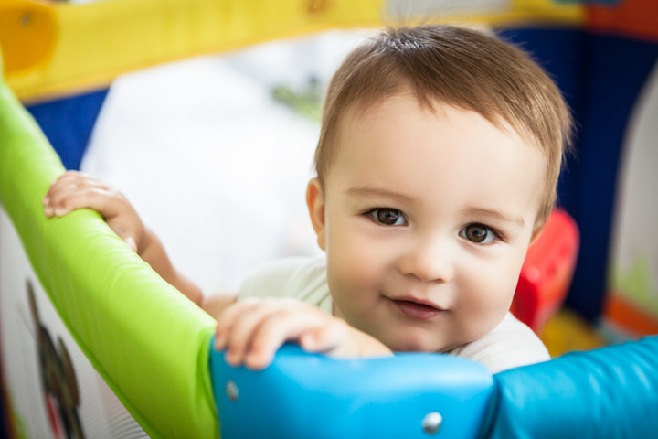 A toddler holds onto brightly colored playground equipment.