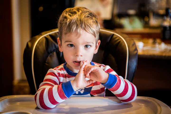 A child in a striped shirt sits at a table with hands near their face.