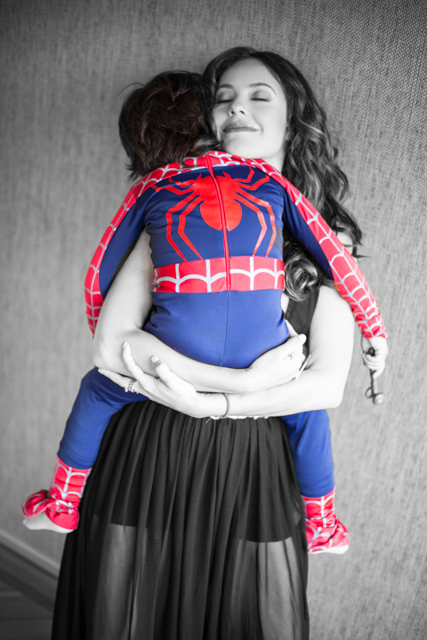 A woman carries a child wearing a bright superhero costume.