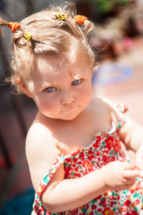 A toddler in a floral dress looks to the side outdoors.