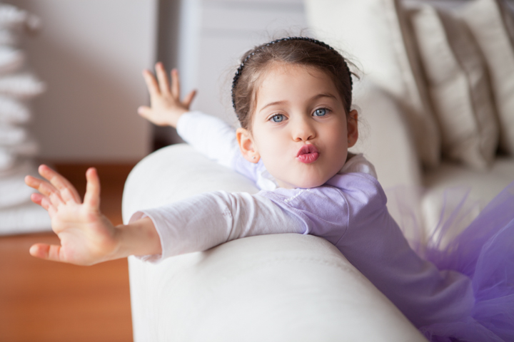 A child in a purple dress stretches both arms across a sofa.