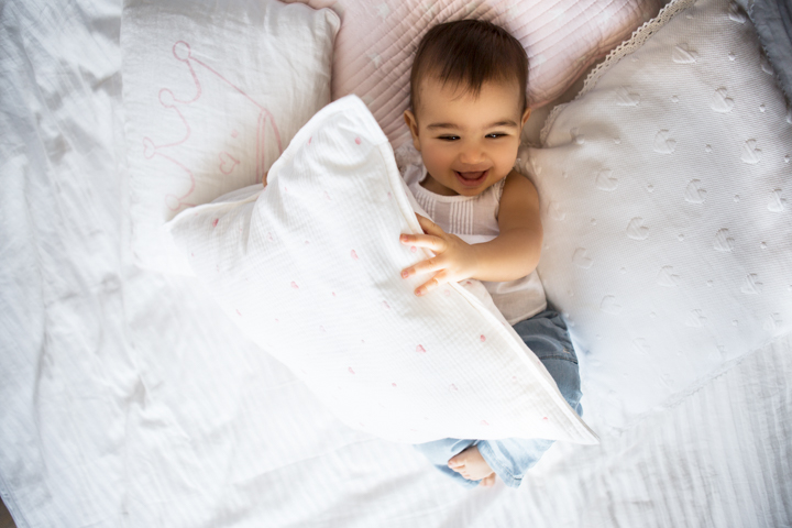 A smiling baby peeks out from beneath a white duvet.