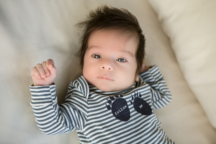 A baby in a striped outfit lies on a soft white blanket.