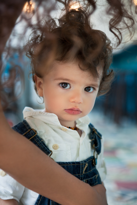 A curly-haired toddler rests in an adult's arms.