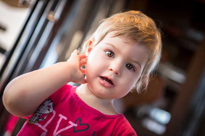 A young child in a red T-shirt holds a hand beside their ear.