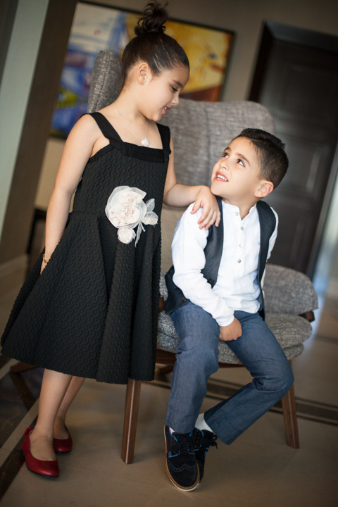 A woman in a black dress stands beside a child dressed in a vest and tie.
