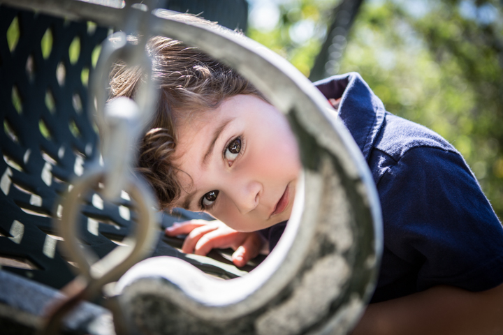 A child peers through decorative metalwork in an outdoor chair.