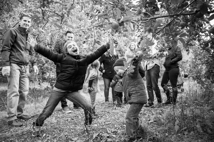 An adult and child jump with their arms raised beneath autumn trees in black and white.