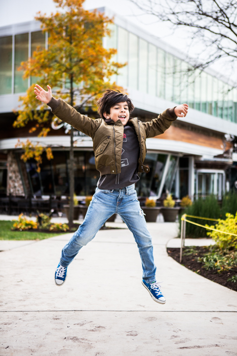 A child jumps with arms spread beside a colorful outdoor railing.