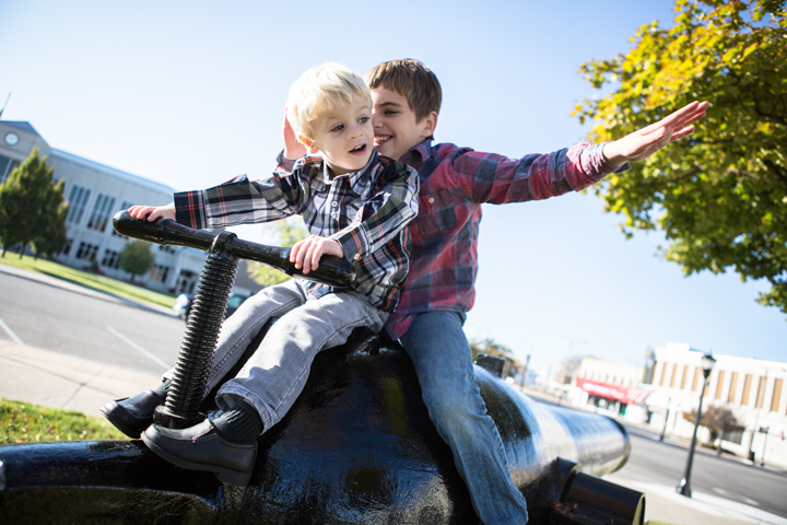 An adult and child stretch their arms while sitting on playground equipment.