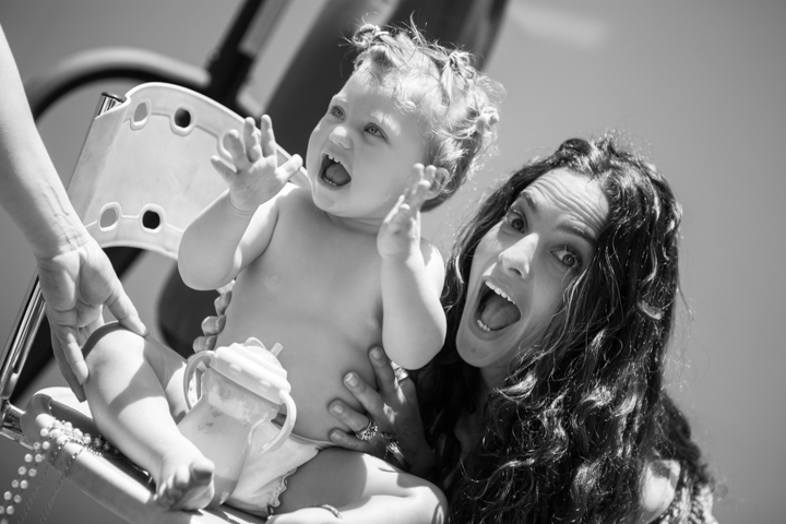 A laughing woman and toddler sit beside a pool in black and white.