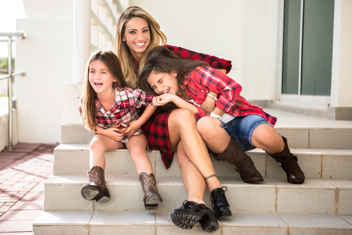 A smiling woman and two children sit close together on outdoor steps.