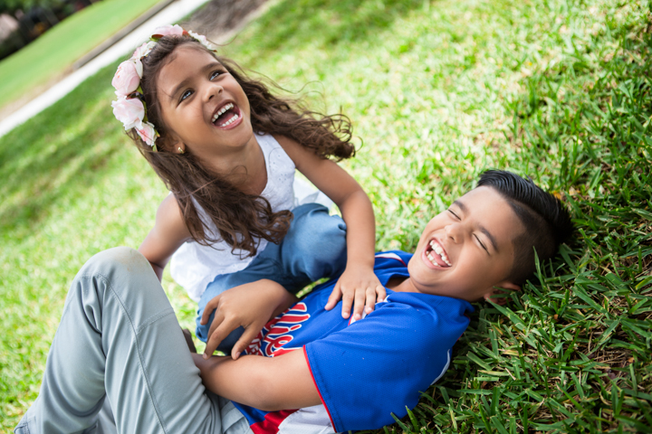 Two laughing children lie together on green grass.