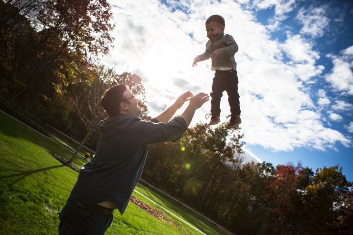 An adult lifts a small child high beneath a bright sky.