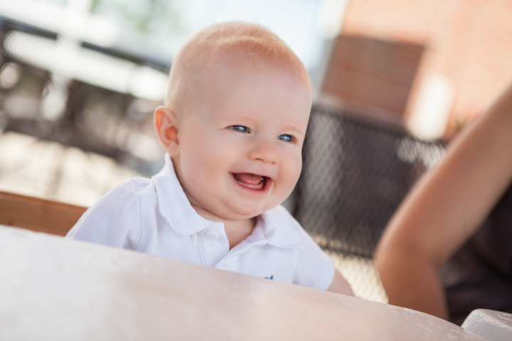 A laughing baby in white sits beside a pale table.